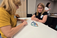 Uczestnicy siedzą przy stole i układają patyczki.