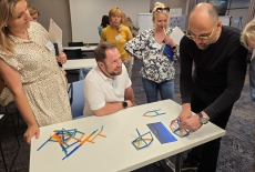 Uczestnicy siedzą przy stole i układają patyczki.